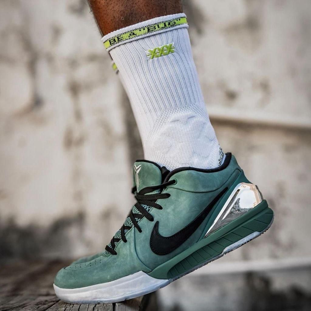 64fb1db6-8691-41f3-b93c-d579ff2c35c7 Close-up of a mint-green high-top Nike basketball shoe with a black swoosh, worn with a white sock featuring yellow-green accents, on a wooden surface.