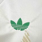 Close-up of white textured fabric featuring a green Adidas trefoil logo embroidered on the material.