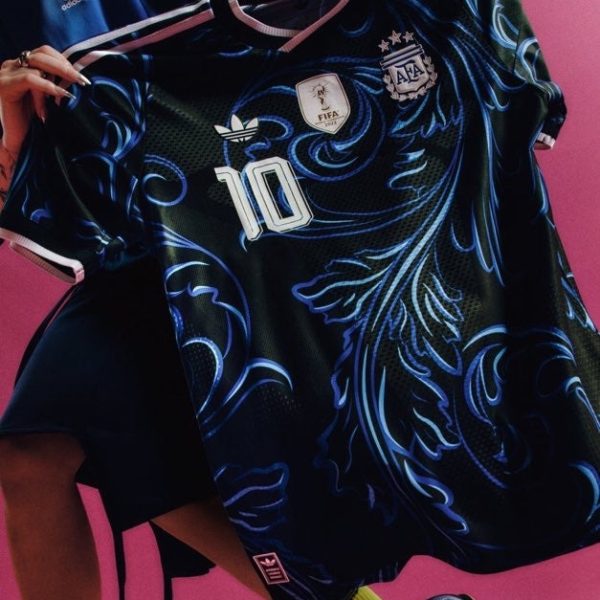 Person holding a dark blue Argentina soccer jersey with number 10, FIFA badge, and team crest against a pink background.