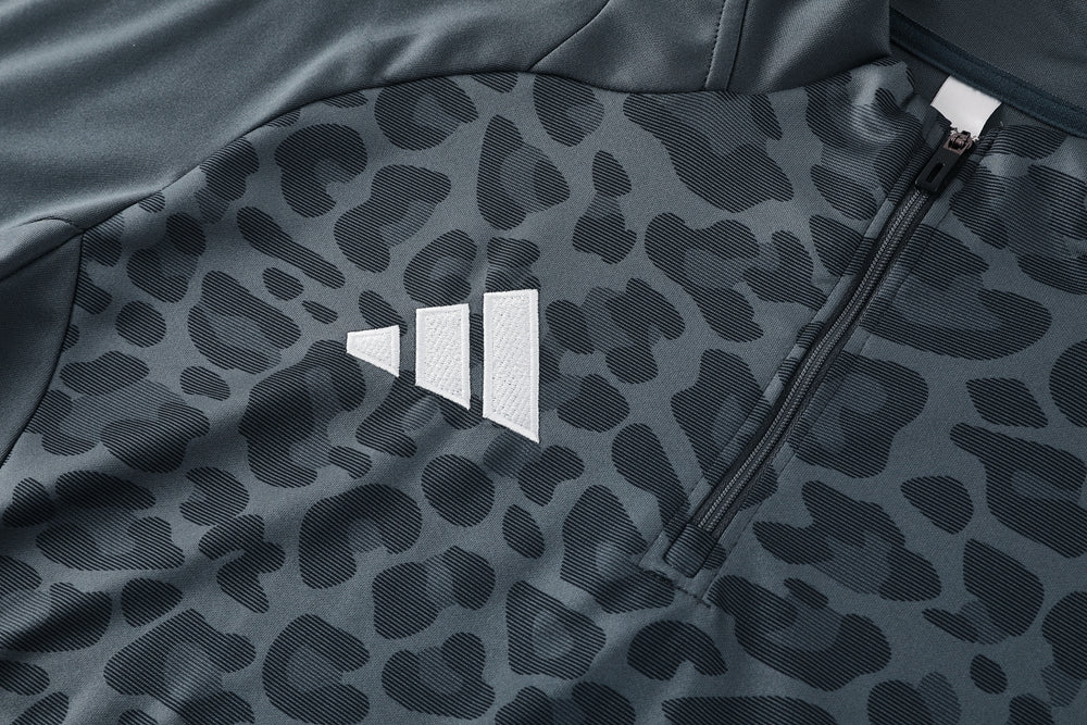 657d611a | UAE SPORT STORE Close-up of a dark patterned fabric jacket with the white Adidas trefoil/three-stripe logo and a zipper nearby, indicating branding on athletic wear.