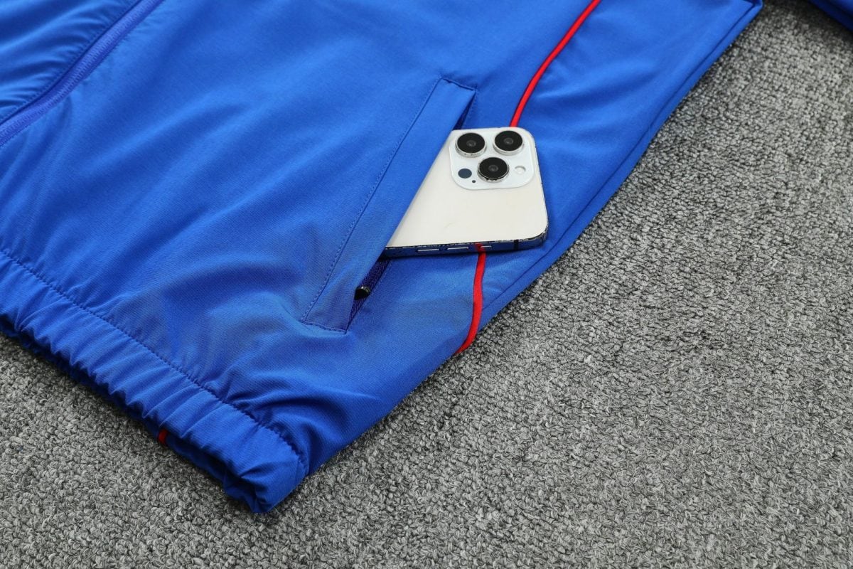 White iPhone with triple rear cameras partially tucked into a blue jacket pocket on a gray carpeted floor