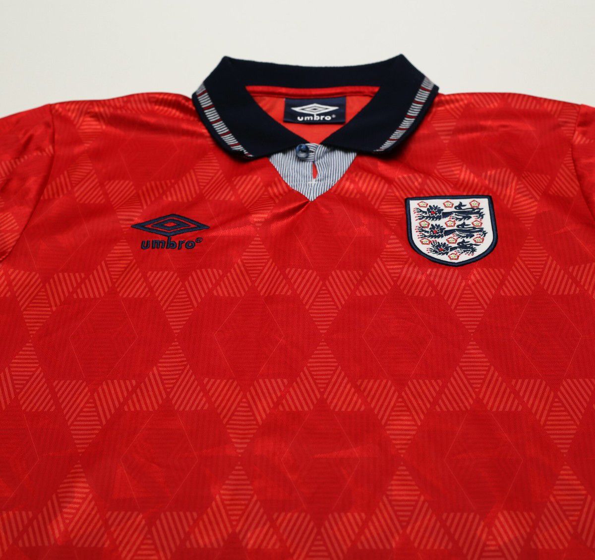 6617e66d-5e55-4b83-b6f2-7d65f6daaca9 | UAE SPORT STORE Red England football jersey with a dark navy collar, Umbro logo on the chest, and the England crest on the opposite side.