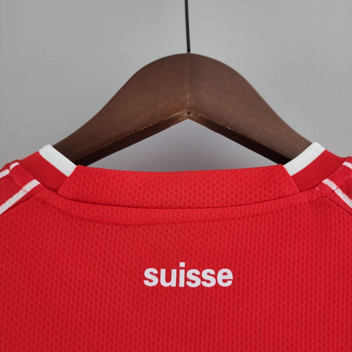 Close-up of a red textured shirt on a wooden hanger, with white text showing the word 'Suisse' partially visible.