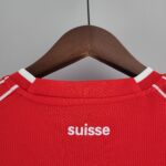 Close-up of a red textured shirt on a wooden hanger, with white text showing the word 'Suisse' partially visible.