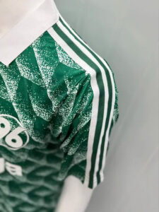 Close-up of a green patterned sports jersey with a white collar and three white stripes along the shoulder/sleeve edge.