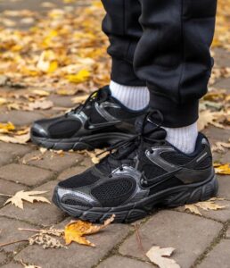 Close-up of black athletic sneakers with gray accents on a brick path, autumn leaves scattered around.