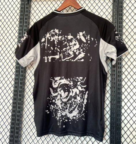 Black T-shirt with gray sleeves hangs on a wooden hanger against a metal grid wall; white abstract print covers the back area.