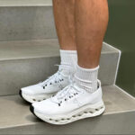 66e387ab-8fad-45c2-93e2-b7cdd30b810f | UAE SPORT STORE White athletic sneakers with a chunky wavy sole on gray concrete stairs, worn with white crew socks.