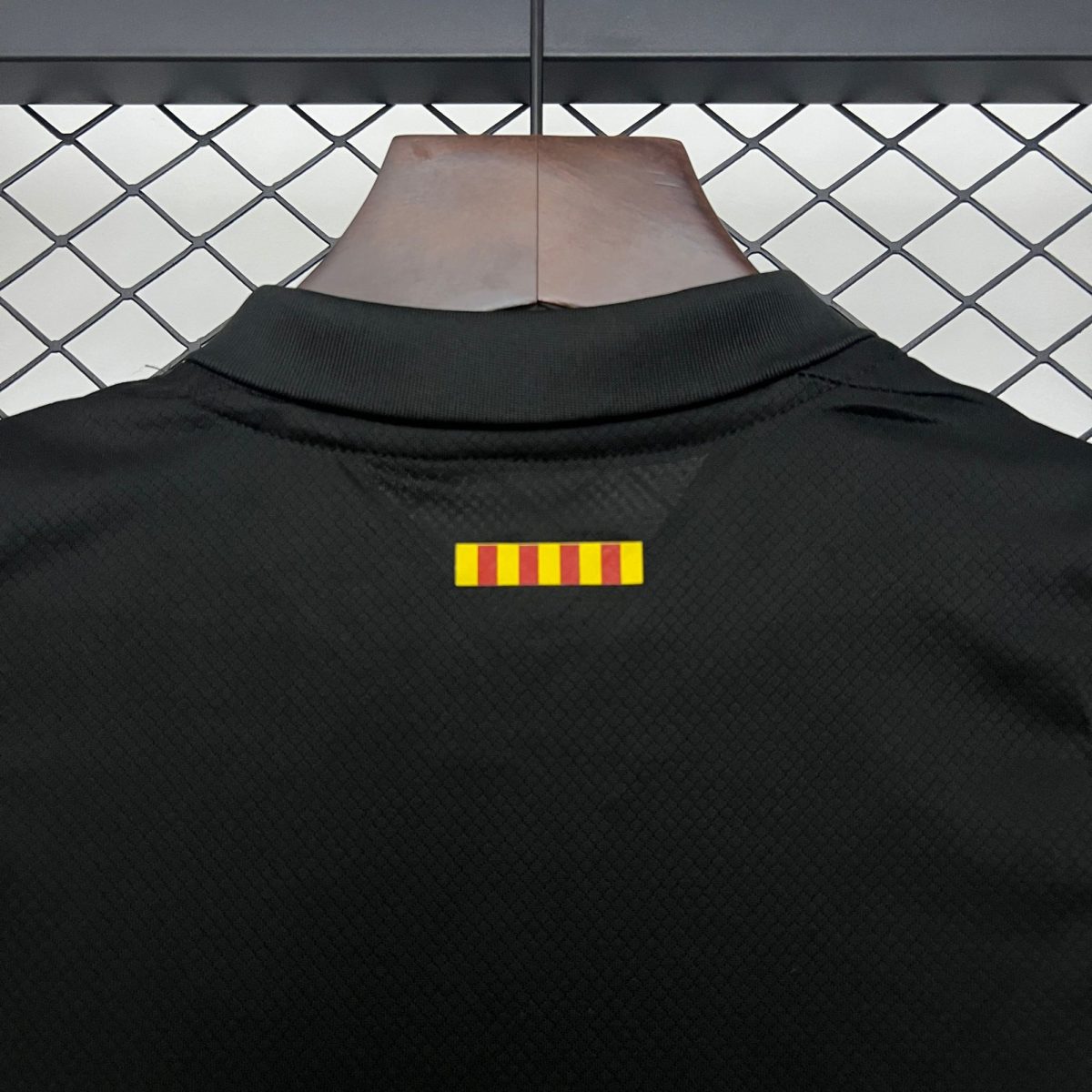 Close-up of a black jacket on a brown display neck in front of a chain-link fence; a small yellow-and-red striped tag is on the chest area.