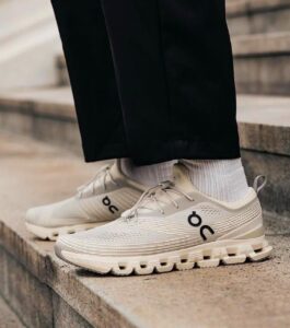 Beige athletic sneakers with ON logo worn with light socks, standing on concrete steps.