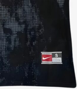 Close-up of dark fabric with a small Nike swoosh logo patch and a white 'S' badge nearby.