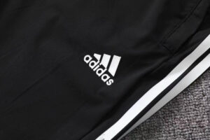 Black Adidas track pants with white logo and side white stripes on a gray carpet background.