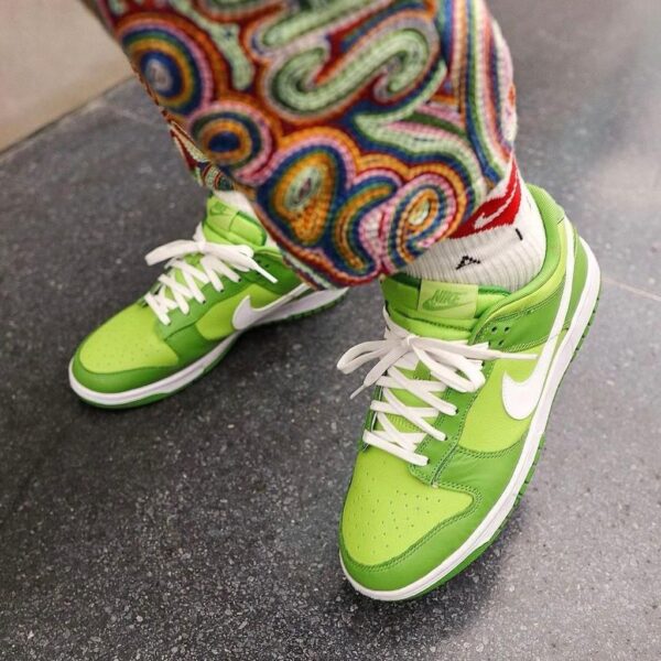Bright lime-green Nike sneakers with white laces on a speckled gray floor, colorful patterned pants partially covering the ankles.
