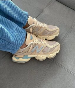 68d9ff3c-e1ff-4da6-81b8-5e832059f630_732856cb-40c2-43b0-92ed-3e4f388e7826 | UAE SPORT STORE Beige sneakers with light blue accents worn with blue corduroy pants, resting on a gray couch surface.