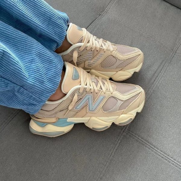 Beige sneakers with light blue accents worn with blue corduroy pants, resting on a gray couch surface.