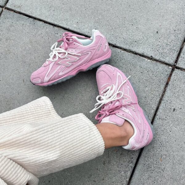 Pair of pink sneakers with white laces resting on a concrete sidewalk, worn with light cream ribbed pants.