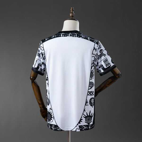 Back view of a white shirt with black tribal print along the shoulders, sides, and sleeves, displayed on a dress form.