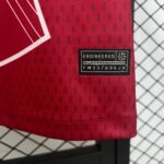 Close-up of red fabric with a black sewing label reading ENGINEERED, against a chain-link fence background.