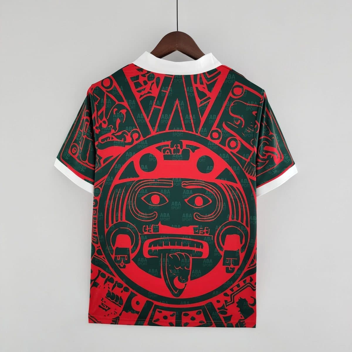 A stylish shirt on a wooden hanger, white collar tips visible, red and green abstract pattern across the garment, plain light background.