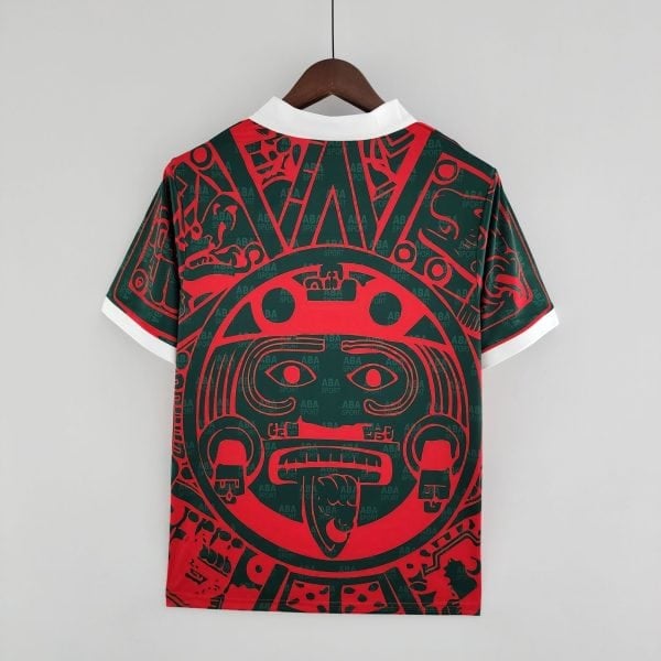 A stylish shirt on a wooden hanger, white collar tips visible, red and green abstract pattern across the garment, plain light background.