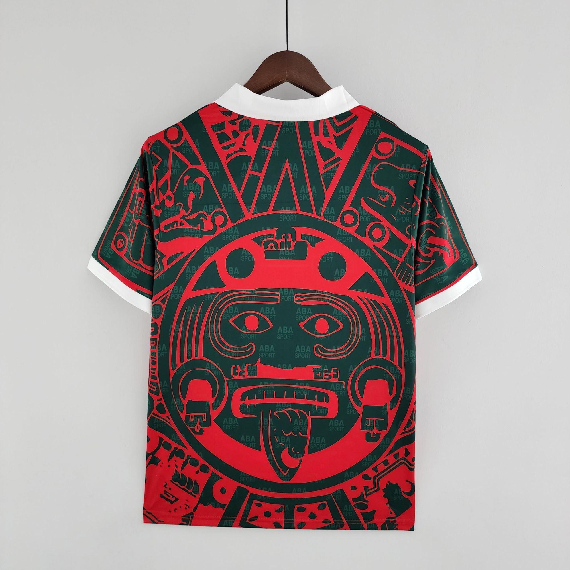 69d59075_6073ef04-72cf-48c6-a264-c2edb0c2d12f | UAE SPORT STORE A stylish shirt on a wooden hanger, white collar tips visible, red and green abstract pattern across the garment, plain light background.
