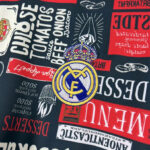 Close-up of a fabric pattern featuring the Real Madrid crest surrounded by various red and white banners and logos.