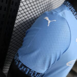 Close-up of a light-blue athletic shirt sleeve with a white Puma logo on the shoulder area, backdrop of a black lattice surface.
