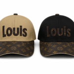 Pair of Louis Vuitton caps: a beige crown with dark brown 'Louis' embroidered, and a black crown with brown 'Louis', both on LV monogram brims.