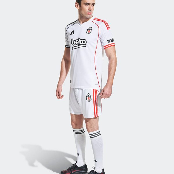 Male model in a white soccer jersey and shorts with red piping, black cleats, standing against a light background.