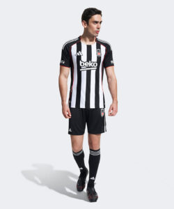 Male model wearing a black-and-white striped soccer jersey with red piping and black shorts, featuring a 'beko' sponsor logo on the chest.
