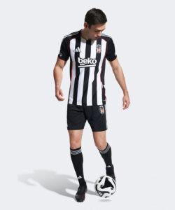 Soccer player in black-and-white striped jersey with sponsor 'beko', standing with a ball at his feet.