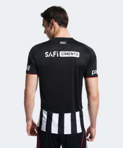 Back view of a man wearing a black soccer jersey with a white 'SAFi CIMENTO' logo on the upper back and black-and-white striped fabric at the waist.