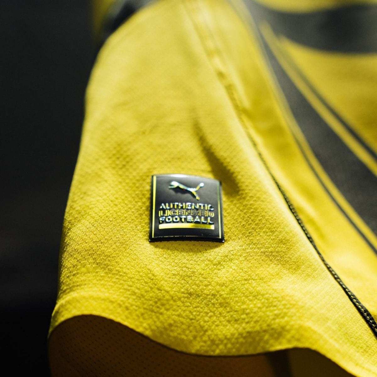 Close-up of yellow fabric with a square patch reading 'AUTHENTIC MICHIGAN FOOTBALL' and a jumping animal logo