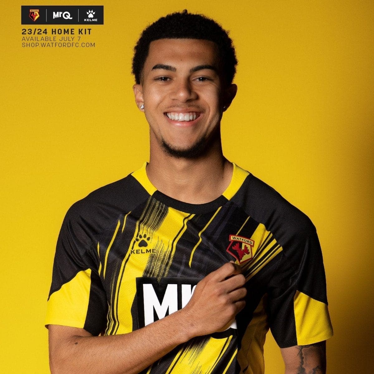 Smiling man in a black and yellow Watford FC jersey against a bright yellow background, crest visible on the chest.