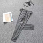 Gray Adidas track pants laid flat for display, showing the logo and tapered cuffs on a gray carpet.