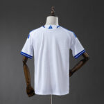 Back view of a white athletic jersey with blue trim on the sleeves and collar, displayed on a mannequin.