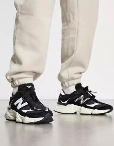 Person wearing beige joggers and black-and-white sneakers standing on a light floor, front view showing the shoes' details.