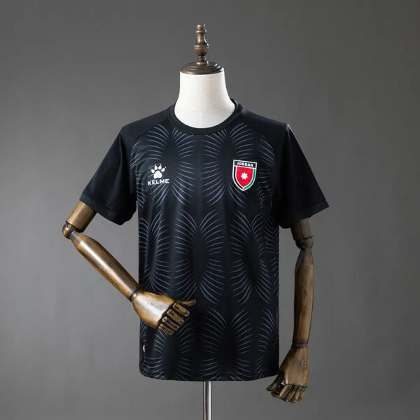 Black athletic jersey on a dress form with crew neck, featuring a white Kelme logo and a red-and-white crest on the chest and curved line pattern across the front.