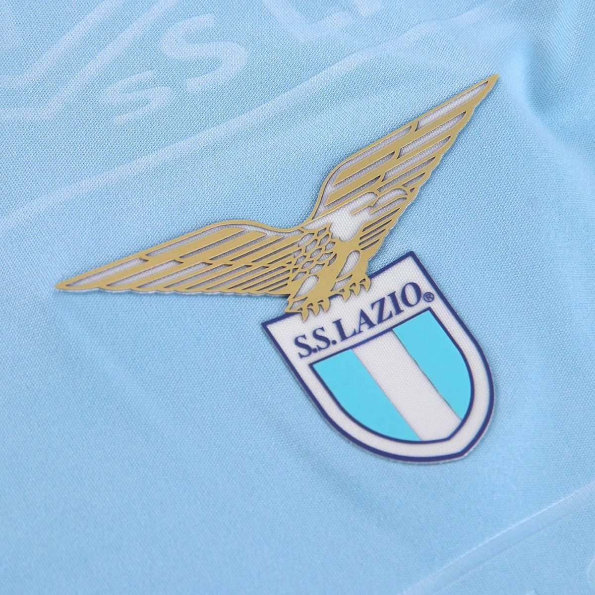 Golden winged-eagle Lazio emblem above the club crest on a light blue jersey.