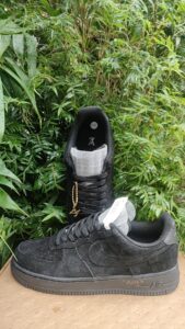Black high-top sneaker with gray tongue and gold chain charm, resting among green bushes outdoors.