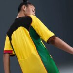 Person wearing a bright color-block sports jersey viewed from the back (yellow sleeves, green panels, black yoke).