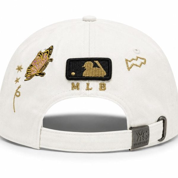 White baseball cap with gold MLB patch on the back, butterfly embroidery and decorative gold accents on the sides, adjustable strap with metal Yankees buckle