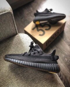 Black Yeezy Boost 350 sneaker resting on a couch with a cardboard shoebox in the background.