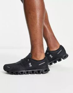Person wearing black On running shoes with a distinctive segmented, cushioned sole on a white background.
