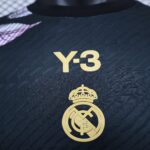 Close-up of a dark jersey with a gold Real Madrid crest embroidered near the bottom.