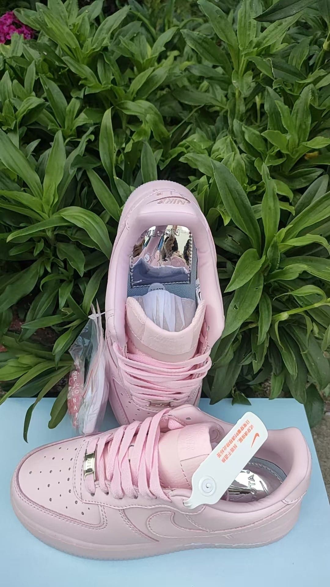 6c8f52e4 | UAE SPORT STORE Pink high-top sneakers displayed on a blue surface with green leafy plants in the background, showcasing the product.