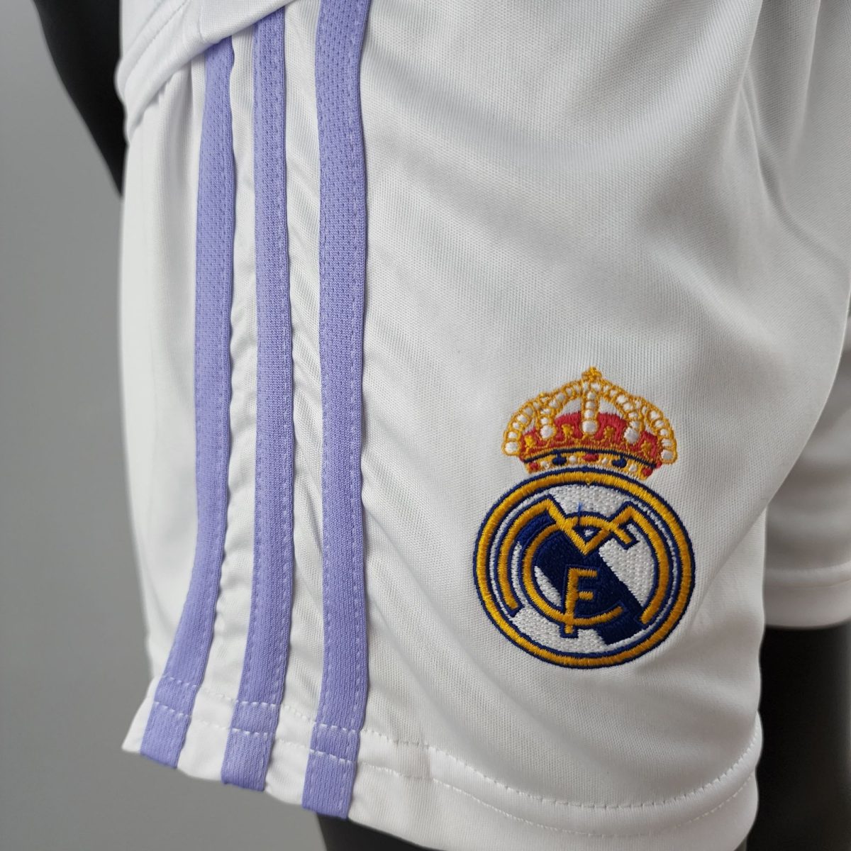 Close-up of a white uniform fabric with purple trim ribbons and a circular embroidered crest in the lower right corner