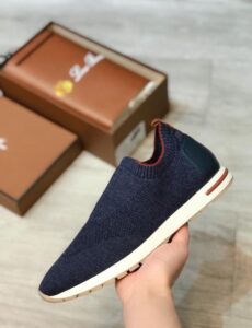 6d37be35-35c0-4a12-96c2-70ea69386db9 | UAE SPORT STORE Navy knit sneaker with a white sole held in hand, brown shoe boxes in the background.