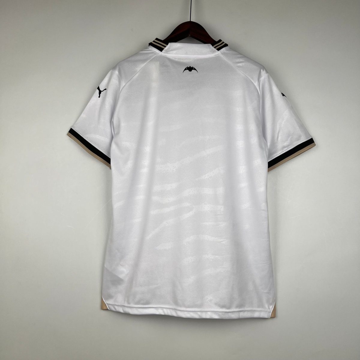 White polo shirt on a hanger, small black bat emblem on the back near the collar, and a Puma logo on the left sleeve.