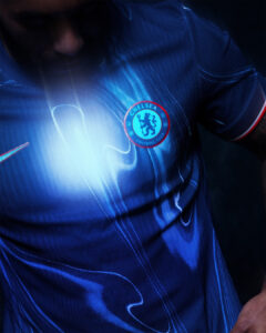 Close-up of a Chelsea FC blue jersey with the club crest on the chest under dramatic lighting.